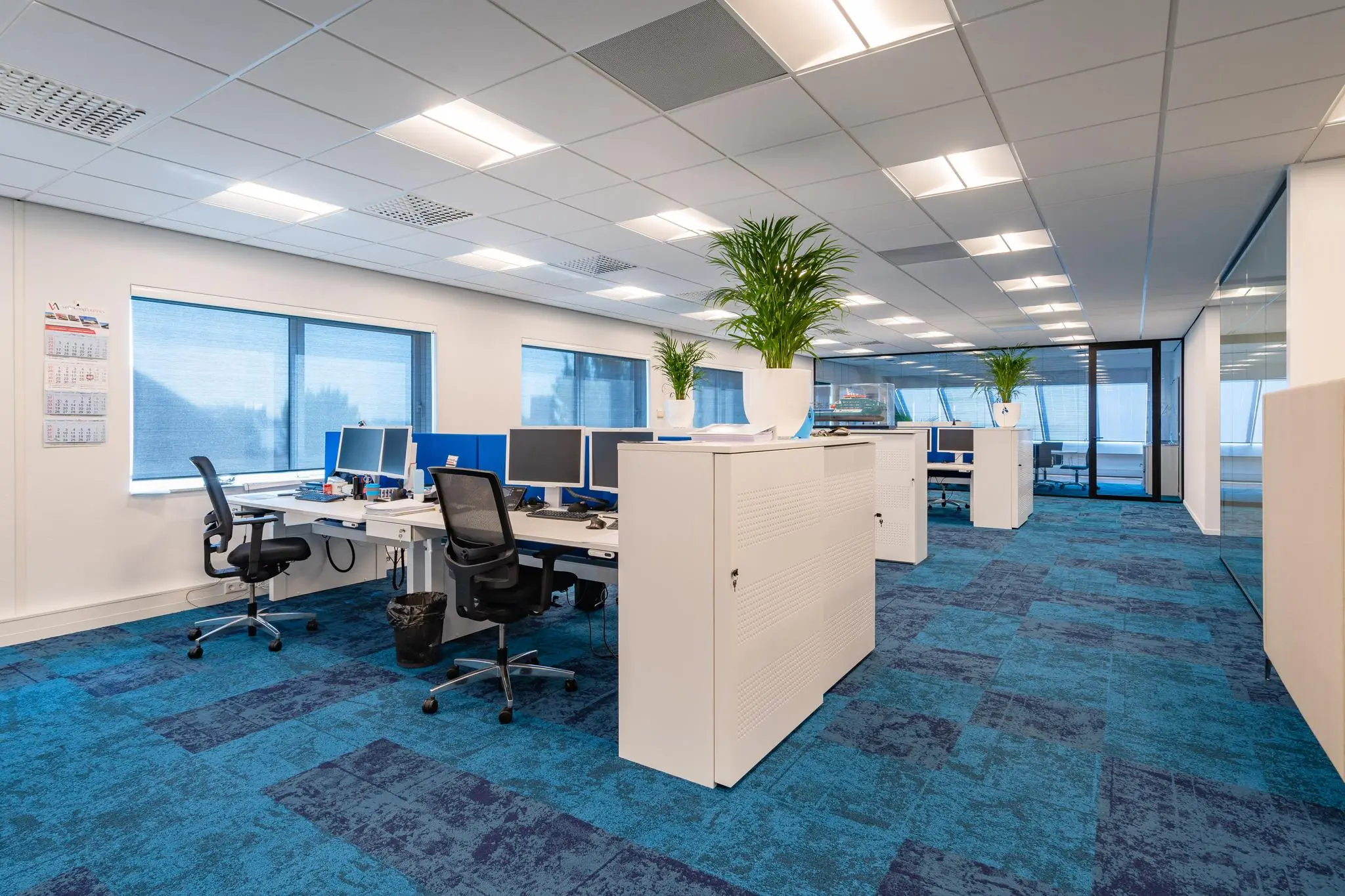 Modern kantoorinterieur aan de Rivium Promenade met open werkplekken, bureaustoelen, computers en blauwe vloerbedekking.